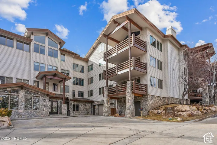 Multi-story building featuring stone and siding exterior, multiple balconies with wood railings, and an integrated garage
