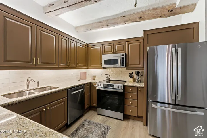 Kitchen featuring wood-finish flooring, stainless steel appliances, granite countertops, tile backsplash, and exposed wood beams
