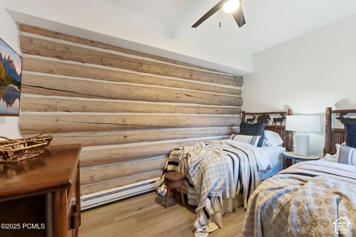 Log-style accent wall, wood-finish flooring, ceiling fan with integrated lighting, and baseboard heating system