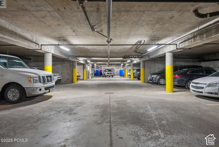 Underground parking garage featuring concrete flooring, exposed overhead piping, and bright overhead lighting