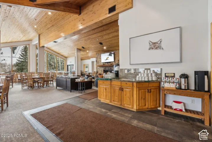 Vaulted wood-finish ceiling with exposed beams, expansive floor-to-ceiling windows, wood-finish cabinetry, stone fireplace, and integrated lighting