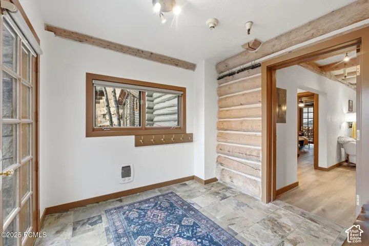 Stone tile flooring, natural wood log wall, natural wood window frame, natural wood trim, and a frosted glass-paneled door