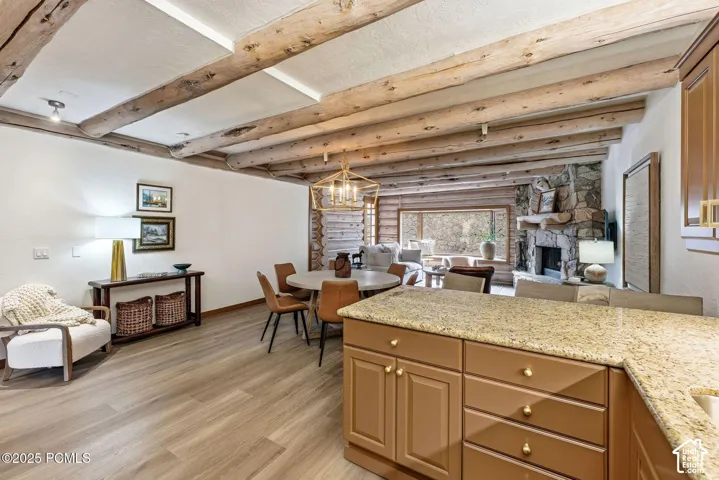 Open-concept living space featuring exposed wooden beam ceiling with recessed lighting, wide-plank wood-finish flooring throughout, and a substantial granite-topped kitchen island with cabinetry