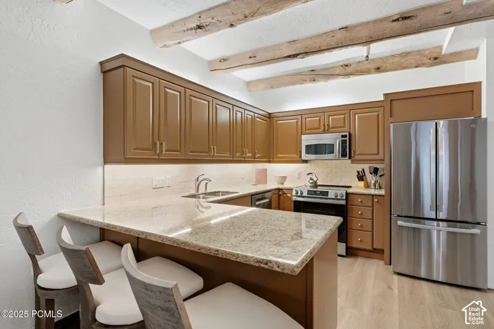 Kitchen with wood-finish flooring, exposed ceiling beams, built-in cabinetry, and stainless steel appliances