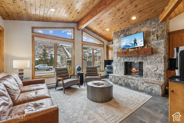 Vaulted wood-paneled ceiling, stone-clad fireplace with wood mantel, large windows with wood trim, and wood-finish flooring