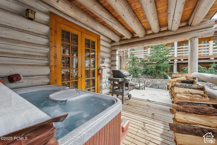 Outdoor hot tub with wood-finish decking, log cabin construction, and exposed wood beam ceiling