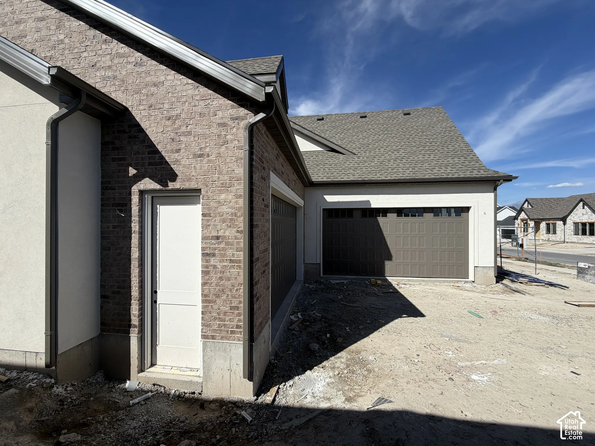 Brick and stucco exterior, asphalt shingle roofing, brown garage door with transom windows, and white side door