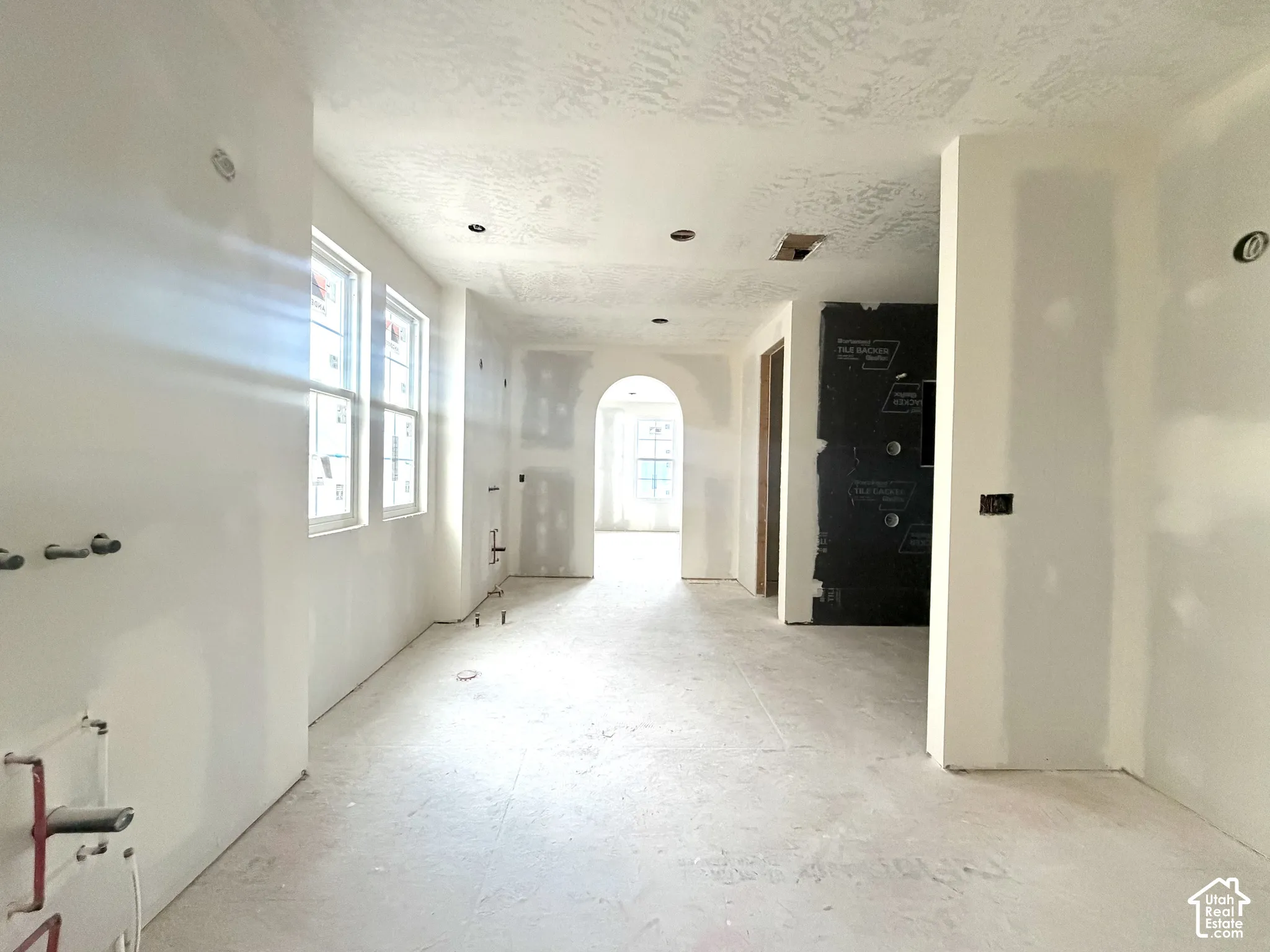 Multiple windows, recessed ceiling lighting, arched doorway, and unfinished flooring