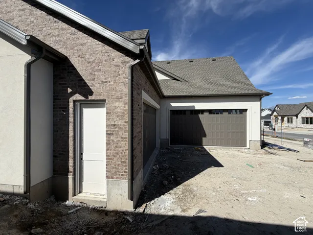 Brick and stucco exterior, asphalt shingle roofing, brown garage door with transom windows, and white side door