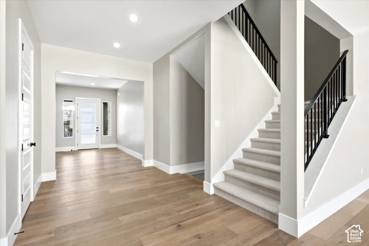 Light wood-finish flooring, recessed lighting, white trim, and a carpeted staircase with black balusters