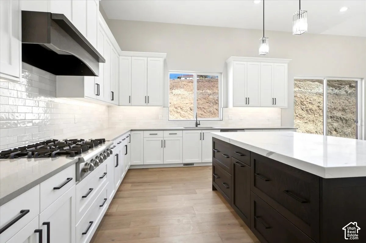 Sleek kitchen featuring white cabinetry, a dark wood-finish island with a light-toned countertop, a professional-grade gas range, and wood-finish flooring