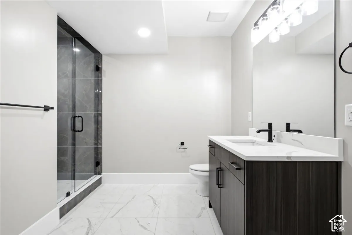 Glass-enclosed shower with dark tile surround, dark wood-finish vanity with countertop, rectangular undermount sink, and matte black fixtures