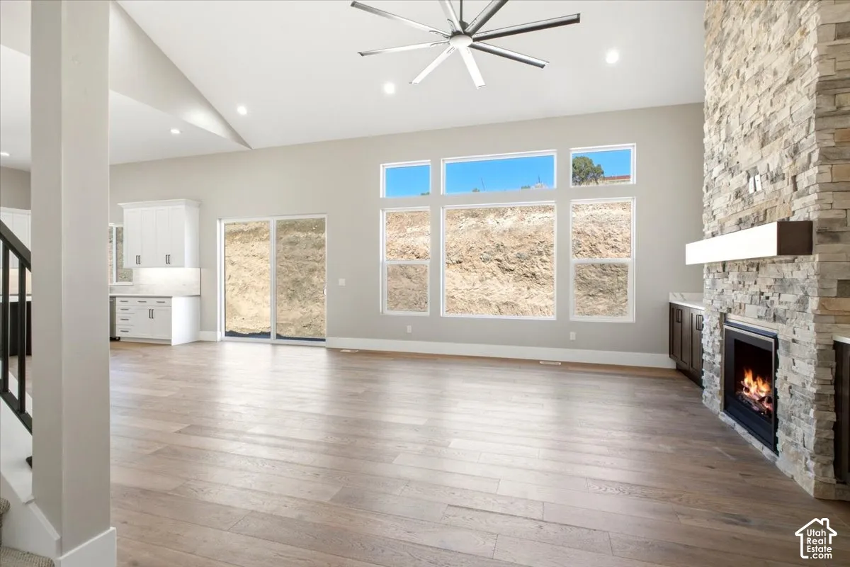 Vaulted ceilings, wood-finish flooring, a stacked stone fireplace with a floating mantel, and a multi-pane window arrangement
