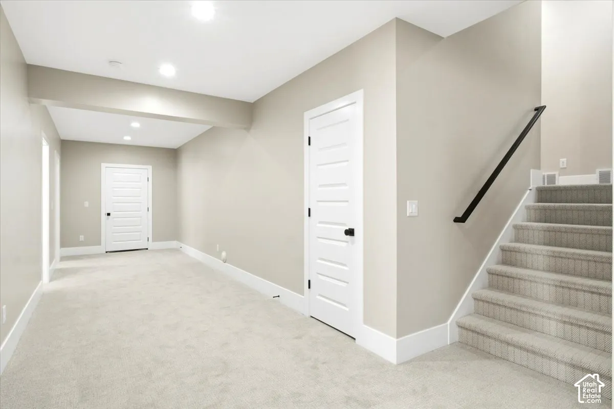 Expansive carpeted area with recessed lighting, multiple entryways, and a staircase featuring a black handrail