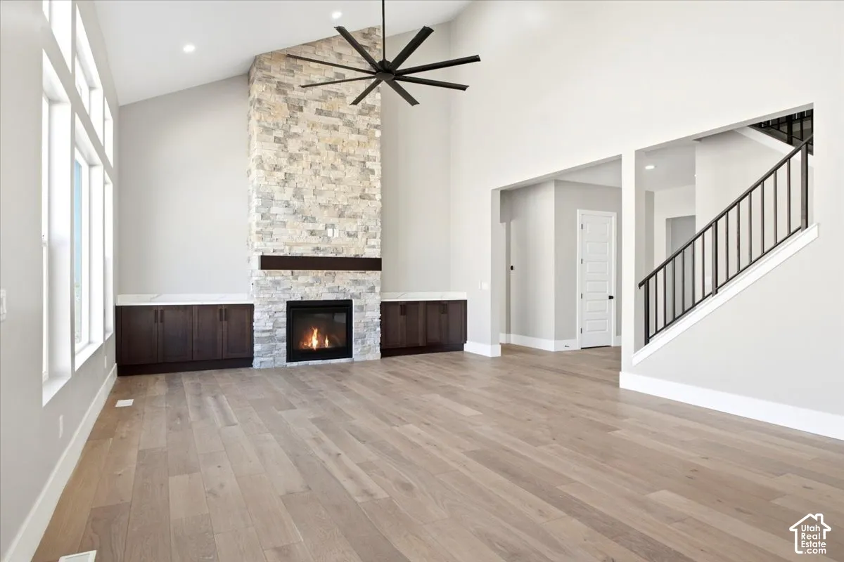 Vaulted ceiling with an architectural ceiling fan, stone-clad fireplace, wood-finish flooring, built-in cabinetry, and a staircase with iron balusters