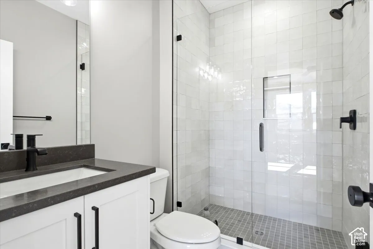 Vanity with a dark countertop and undermount sink, white cabinetry with black hardware, and an expansive glass-enclosed shower with tiled walls and flooring