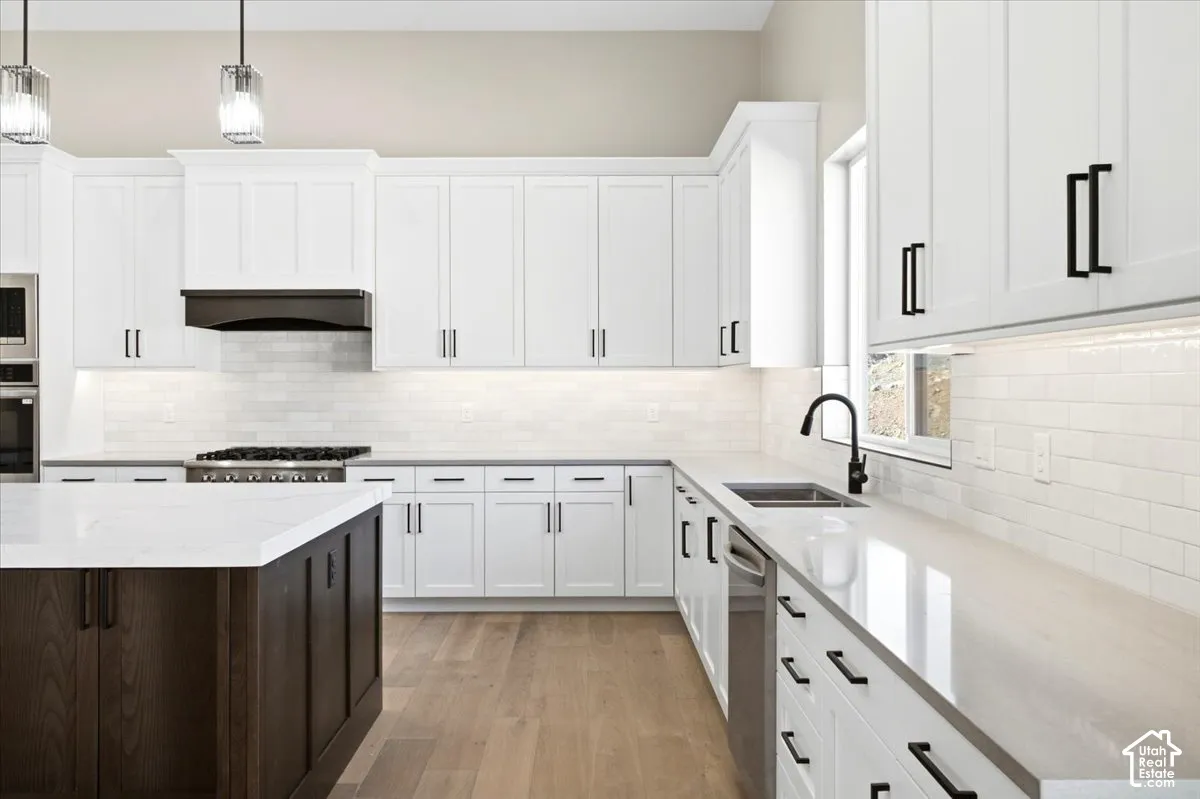 Kitchen featuring white shaker-style cabinetry, a dark wood-finish island, light-toned countertops, and wood-finish flooring