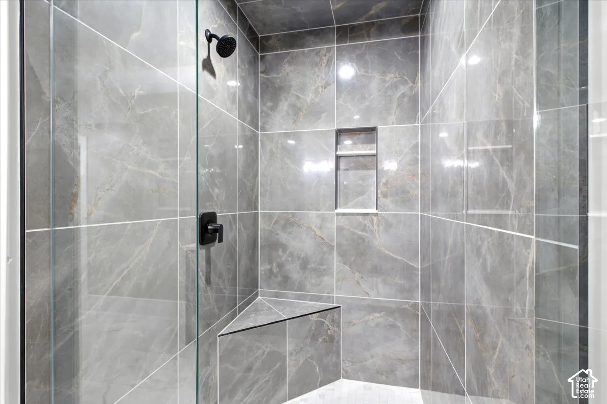 Glass-enclosed shower featuring large format gray marble-look tile, built-in corner bench, recessed shower niche, and matte black fixtures