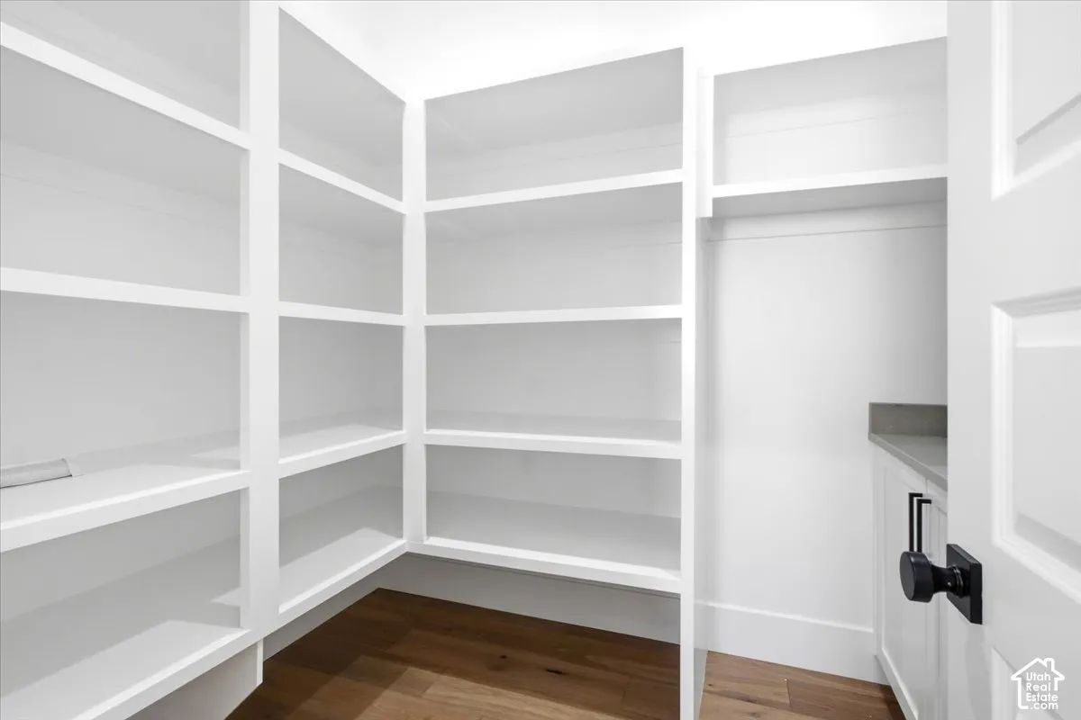 Extensive built-in shelving, wood-finish flooring, white cabinetry, and stone-finish countertop with a matte black cabinet pull