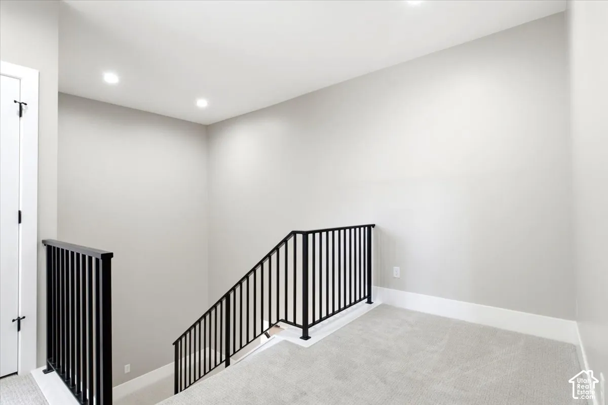 Recessed lighting illuminates the space, featuring black metal balusters and light-toned carpeting