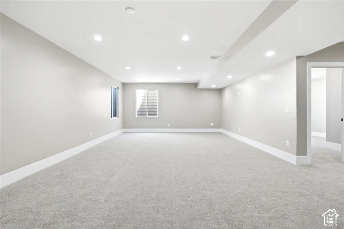 Recessed ceiling lighting illuminates a spacious room featuring light gray carpet flooring