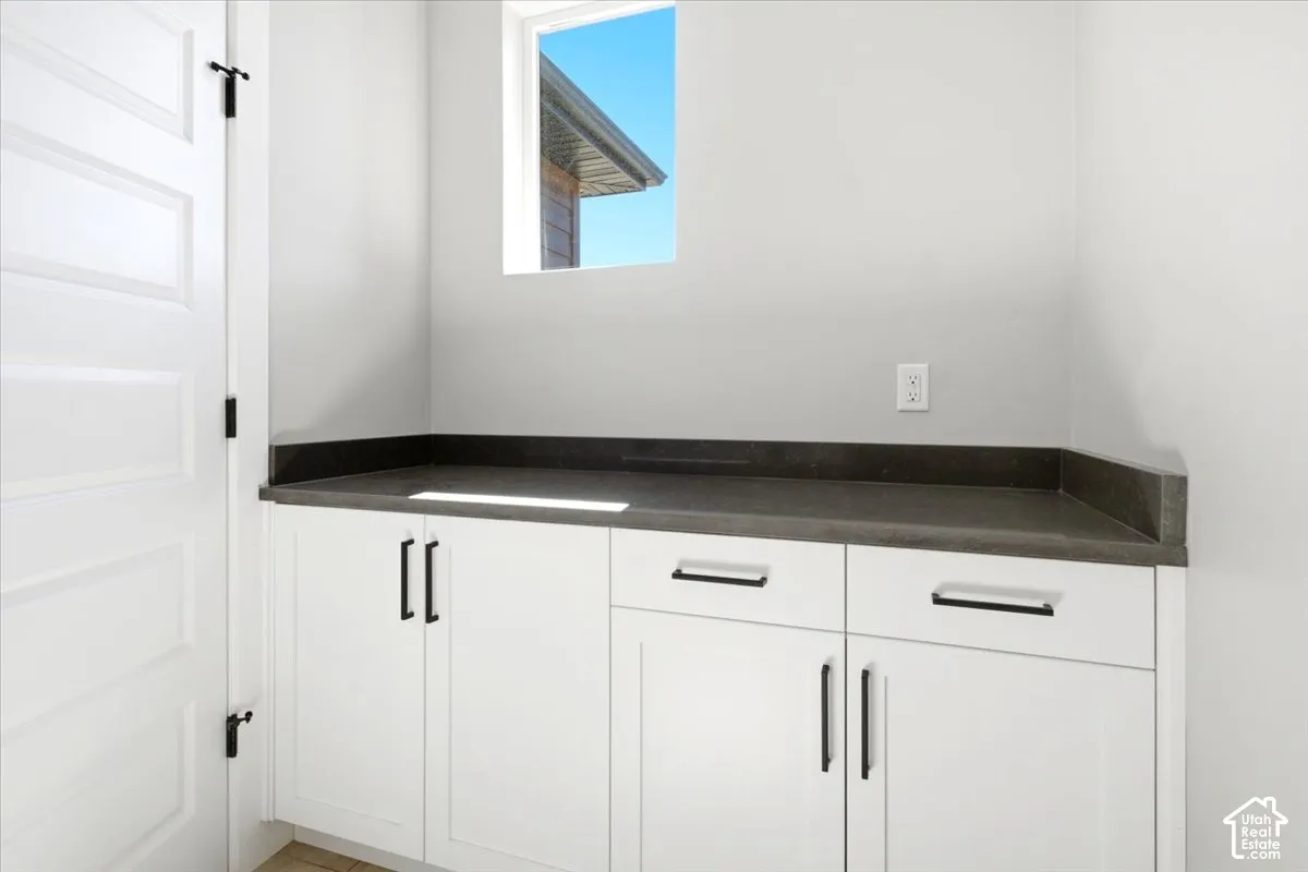 White shaker-style cabinetry with black hardware, dark countertop, and a window