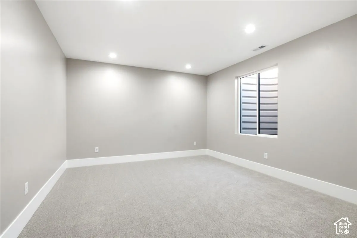 Recessed ceiling lighting, light gray wall paint, white trim, gray carpeting, and a window with a white frame