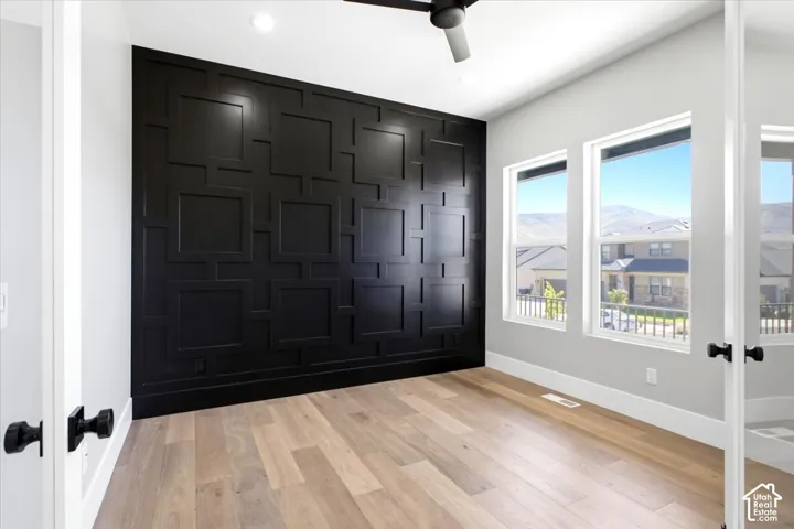 Feature wall with geometric paneling, wood-finish flooring, two large windows, recessed lighting, and a ceiling fan