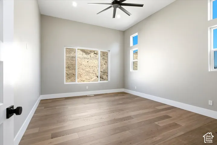 Vaulted ceiling with a ceiling fan, wood-finish flooring, and multiple windows