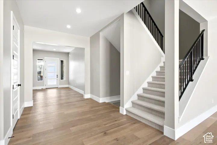 Light wood-finish flooring, recessed lighting, white trim, and a carpeted staircase with black balusters