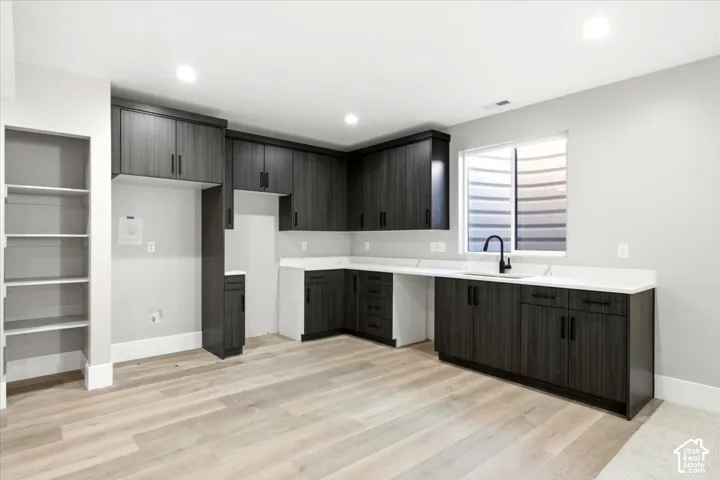 Built-in shelving, wood-finish flooring, dark wood-tone cabinetry, white countertops, and a matte black single-handle faucet