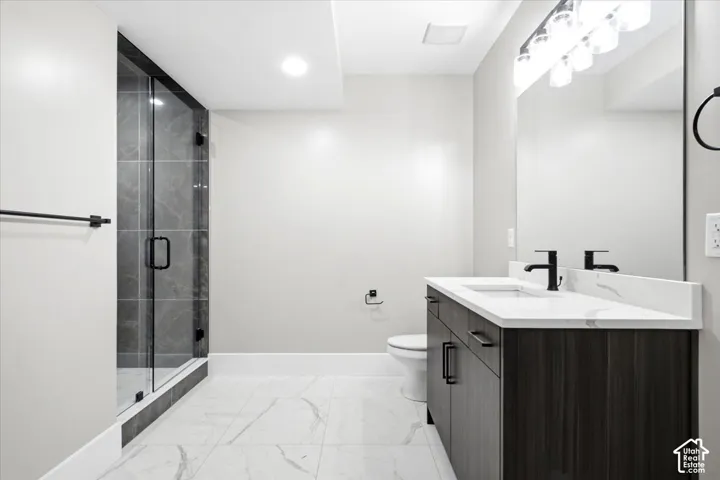Glass-enclosed shower with dark tile surround, dark wood-finish vanity with countertop, rectangular undermount sink, and matte black fixtures