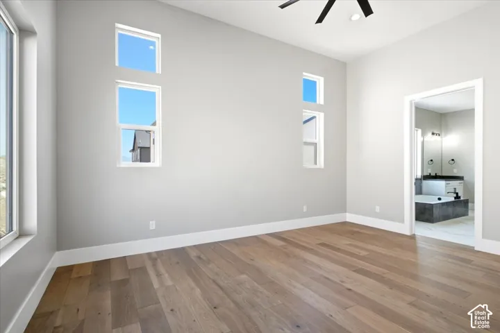 Vaulted ceiling with a contemporary ceiling fan, wood-finish flooring, multiple windows providing natural light, and an en-suite bathroom featuring a built-in soaking tub