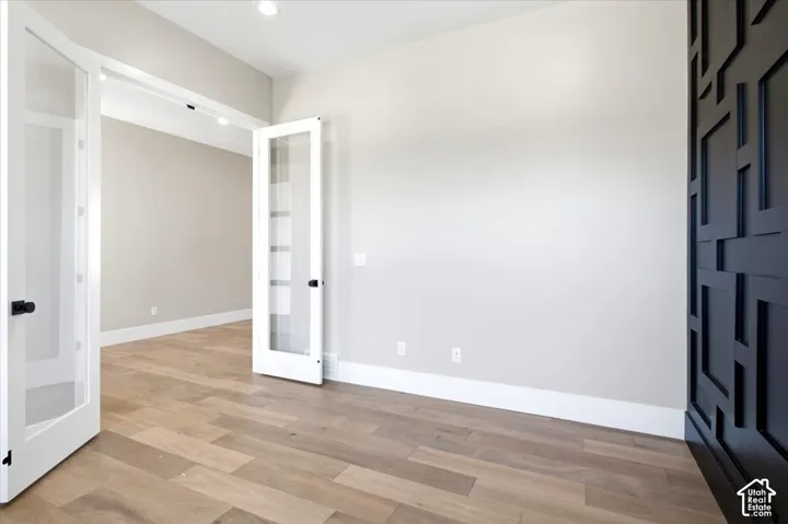French doors with clear glass panels, wood-finish flooring, recessed lighting, and a decorative accent wall