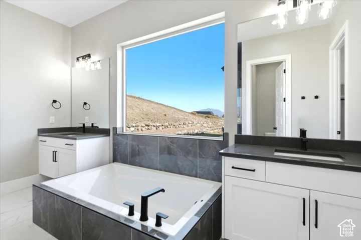 Freestanding soaking tub with dark tile surround, dual white vanities with dark countertops, and large framed window