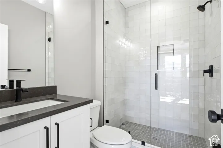Vanity with a dark countertop and undermount sink, white cabinetry with black hardware, and an expansive glass-enclosed shower with tiled walls and flooring