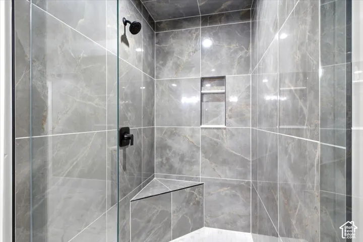 Glass-enclosed shower featuring large format gray marble-look tile, built-in corner bench, recessed shower niche, and matte black fixtures