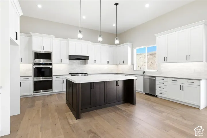 Vaulted ceiling kitchen featuring wood-finish flooring, white cabinetry, a dark-stained island with a light-colored countertop, and stainless steel appliances