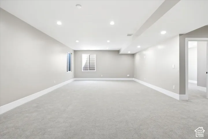 Recessed ceiling lighting illuminates a spacious room featuring light gray carpet flooring