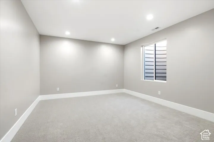 Recessed ceiling lighting, light gray wall paint, white trim, gray carpeting, and a window with a white frame