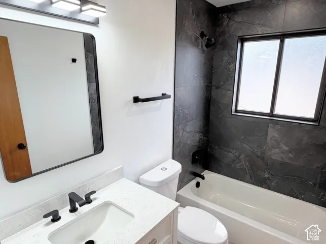 Vanity with white countertop and matte black faucet, dark rectangular mirror, white bathtub with dark tile surround, and matte black shower fixtures