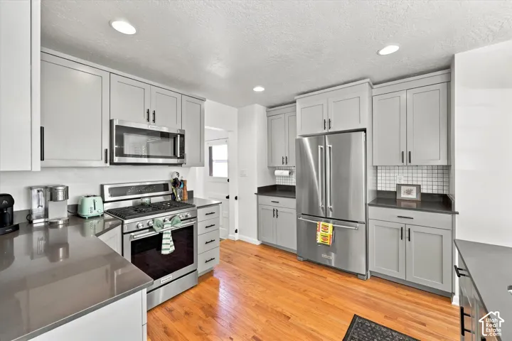Kitchen featuring light gray cabinetry, stainless steel appliances, dark countertops, a white subway tile backsplash, and wood-finish flooring