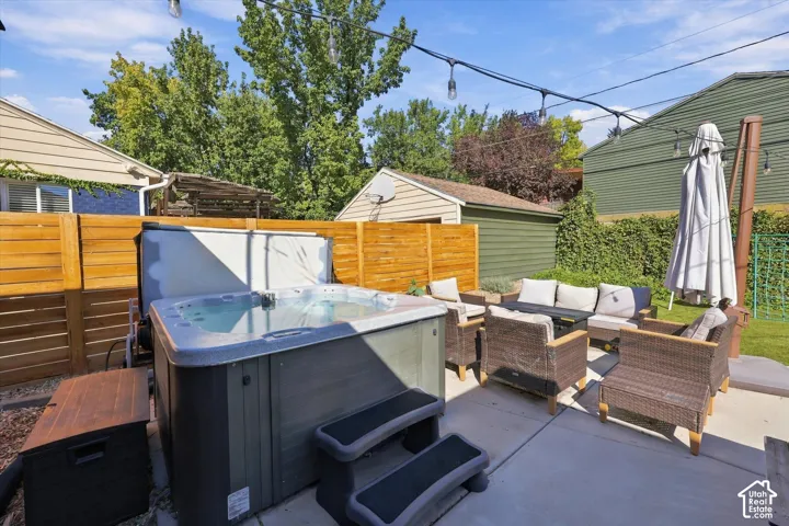 Backyard concrete patio with an integrated hot tub, string lighting, and a horizontal wood privacy fence