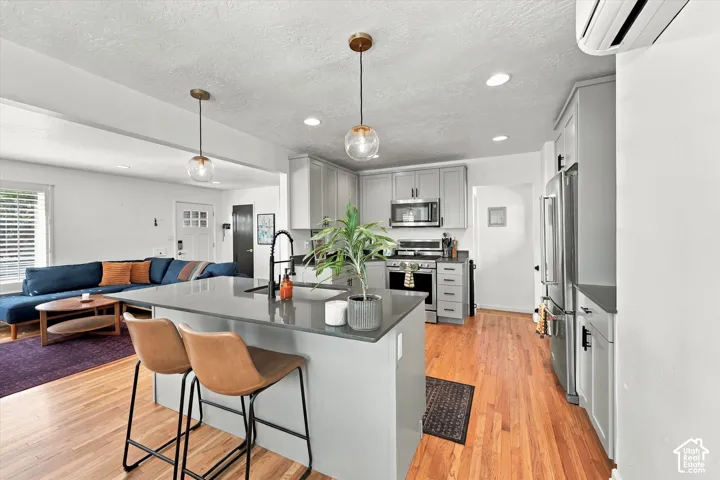 Open-concept kitchen featuring an island with seating, pendant lighting, stainless steel appliances, and light wood-finish flooring