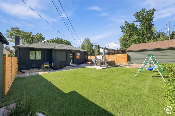 Expansive artificial turf lawn with a patio area, privacy fencing, and a detached structure with horizontal siding