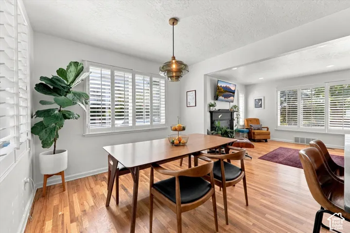 Hardwood flooring, white wall paint, multiple windows with white plantation shutters, built-in fireplace with black mantel, and recessed ceiling lighting
