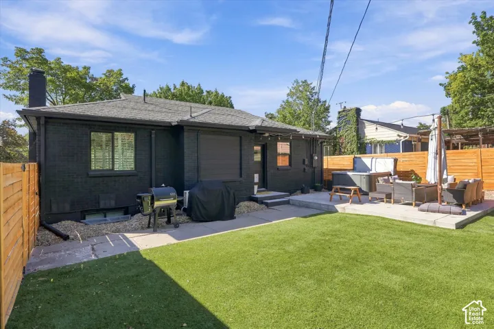 Expansive backyard featuring artificial turf, a concrete patio, a built-in hot tub, and wood fencing