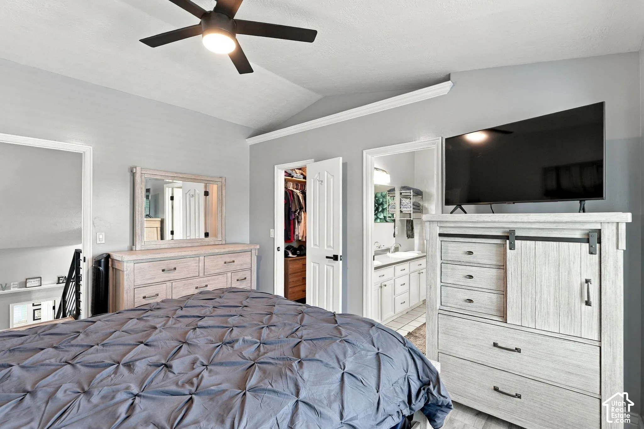 Vaulted ceiling with a ceiling fan, white trim work, light gray painted walls, and wood-finish flooring