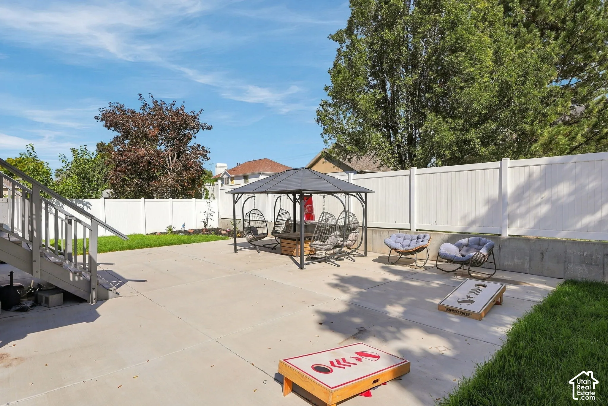 Expansive concrete patio with a permanent gazebo structure, bordered by a white privacy fence and sections of manicured lawn