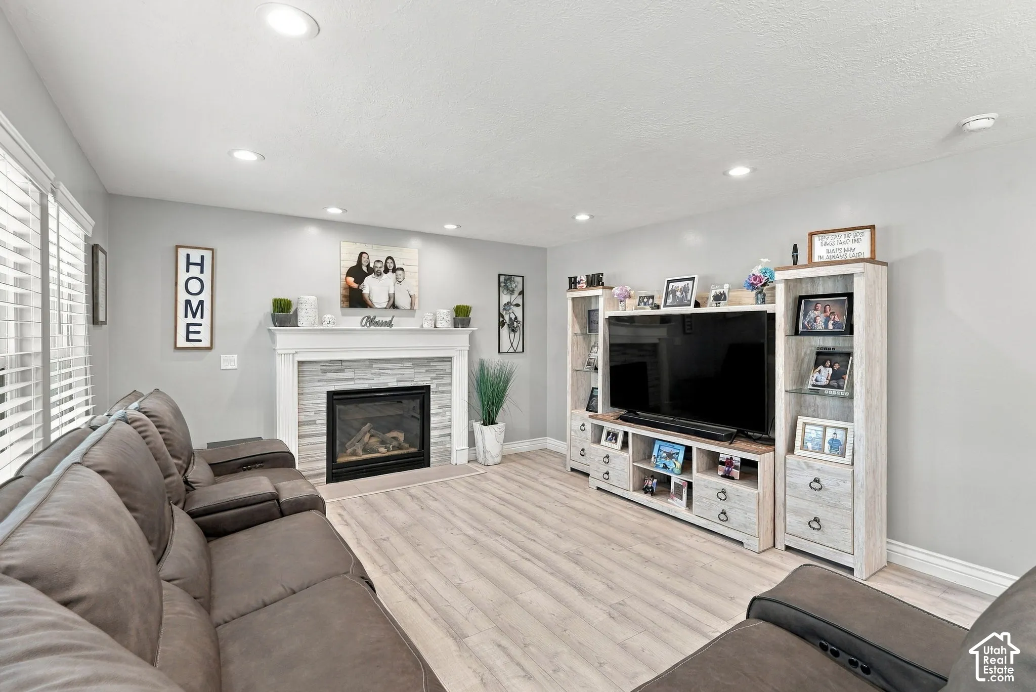 Recessed lighting, wood-finish flooring, fireplace with stone surround, and window with blinds